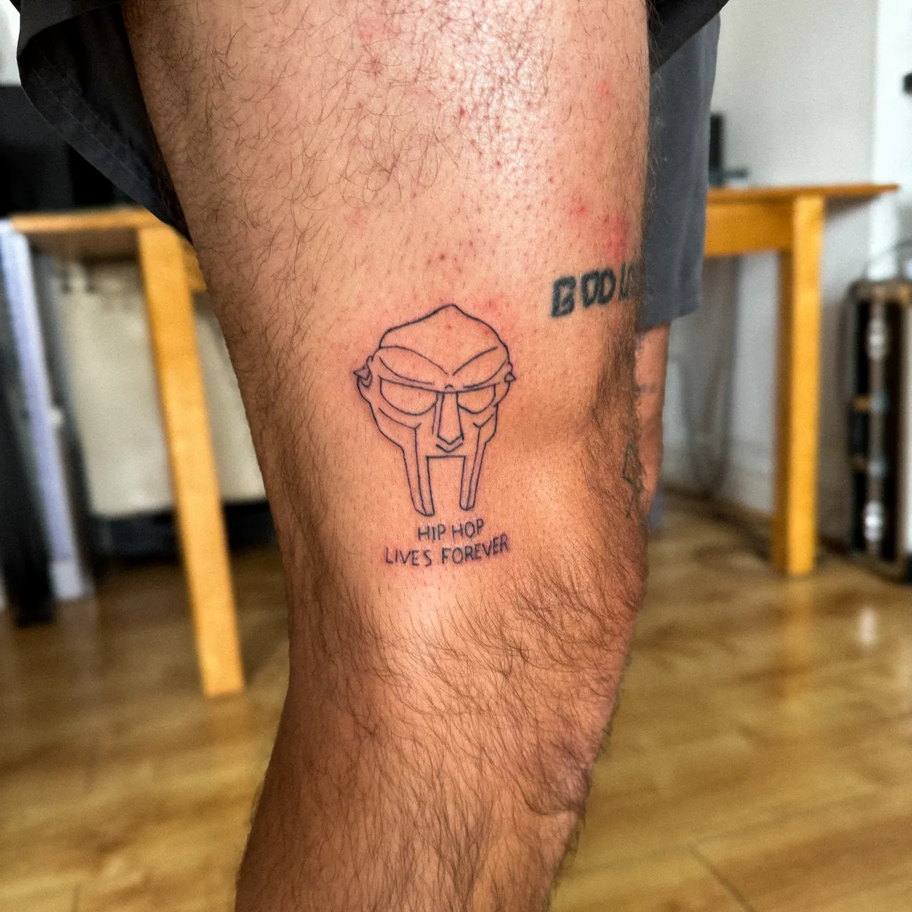 Tatuaje de la máscara de MF DOOM con la leyenda hip-hop lives forever